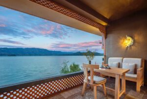 Morning view from the Yuelian Zhuang Dabu Villa lake view room at Lugu Lake, Yunnan, front courtyard facing the lake with Gemu Goddess Mountain reflected on the mirror-like surface, morning mist drifting over the water, an eagle soaring gracefully overhead