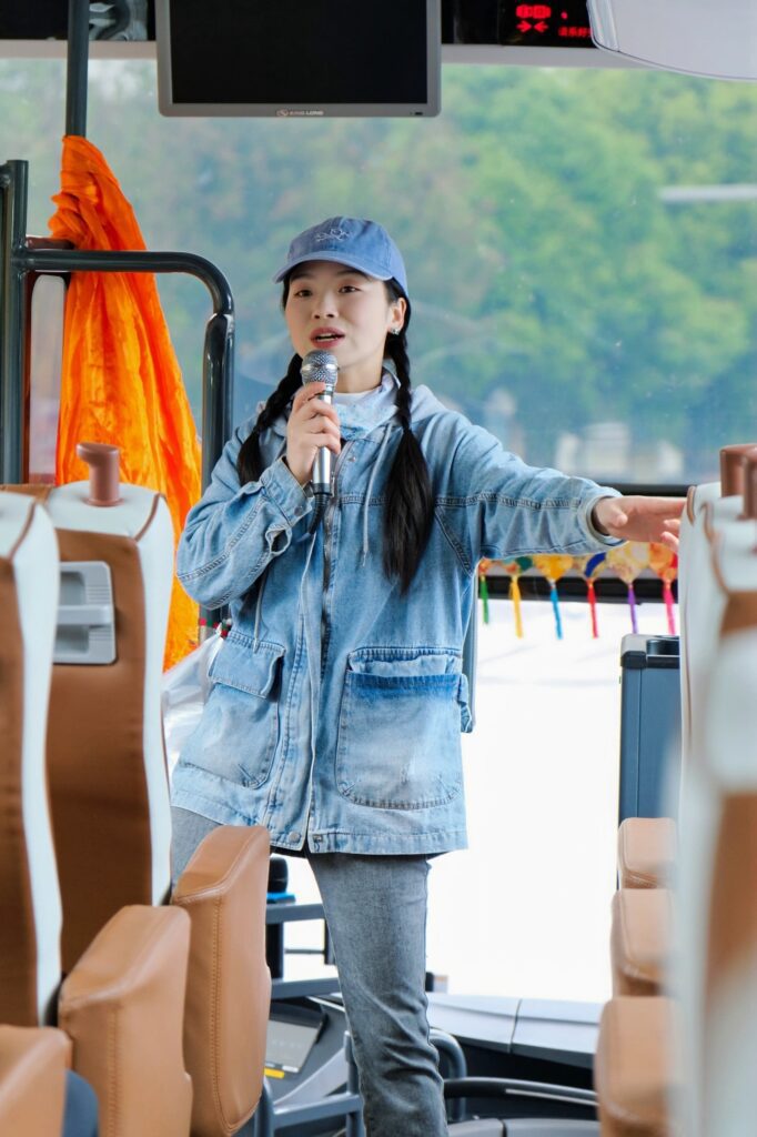 雲南旅遊推薦|昆大麗瀘沽湖8日深度慢遊,最值得的雲南行程 - CITS China International Travel Service CITS 中国国旅 China2Go 云南行程专业持证导游站立旅游巴士走道,手持麦克风向旅客进行景点解说服务,车厢座椅整齐宽敞,车窗外可见沿途绿色山景