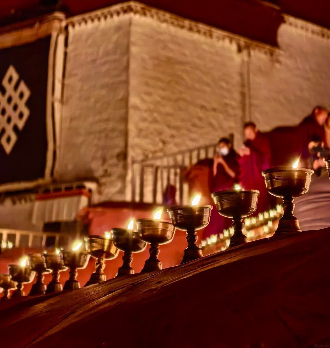 西藏燃燈節甘丹寺夜晚供燈,一排酥油燈前景,僧人在寺牆旁點燈