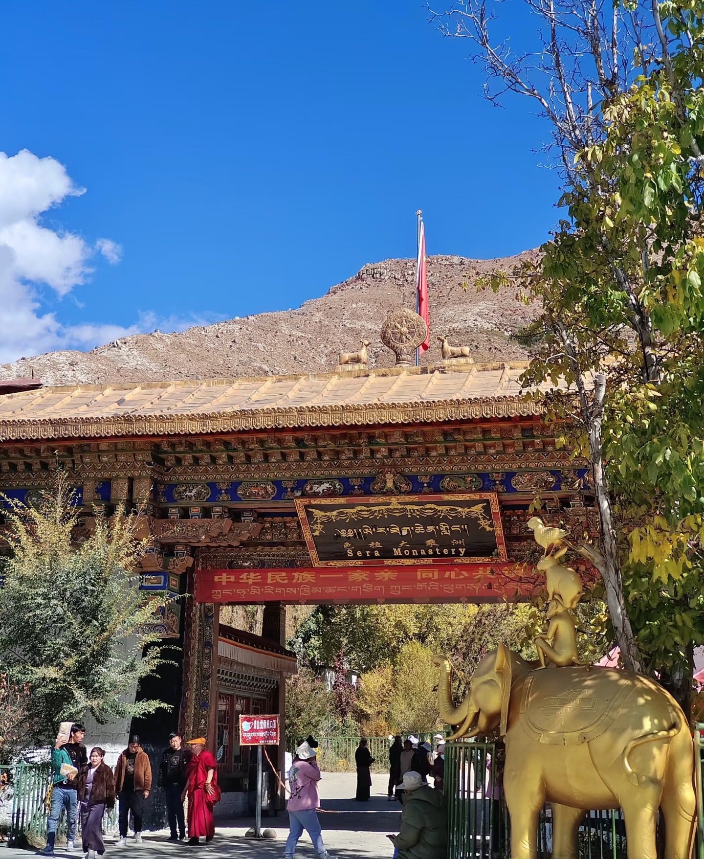 西藏拉薩色拉寺大門入口景觀,展示寺廟匾額、金色法輪與四合友雕像-中國國旅China2Go