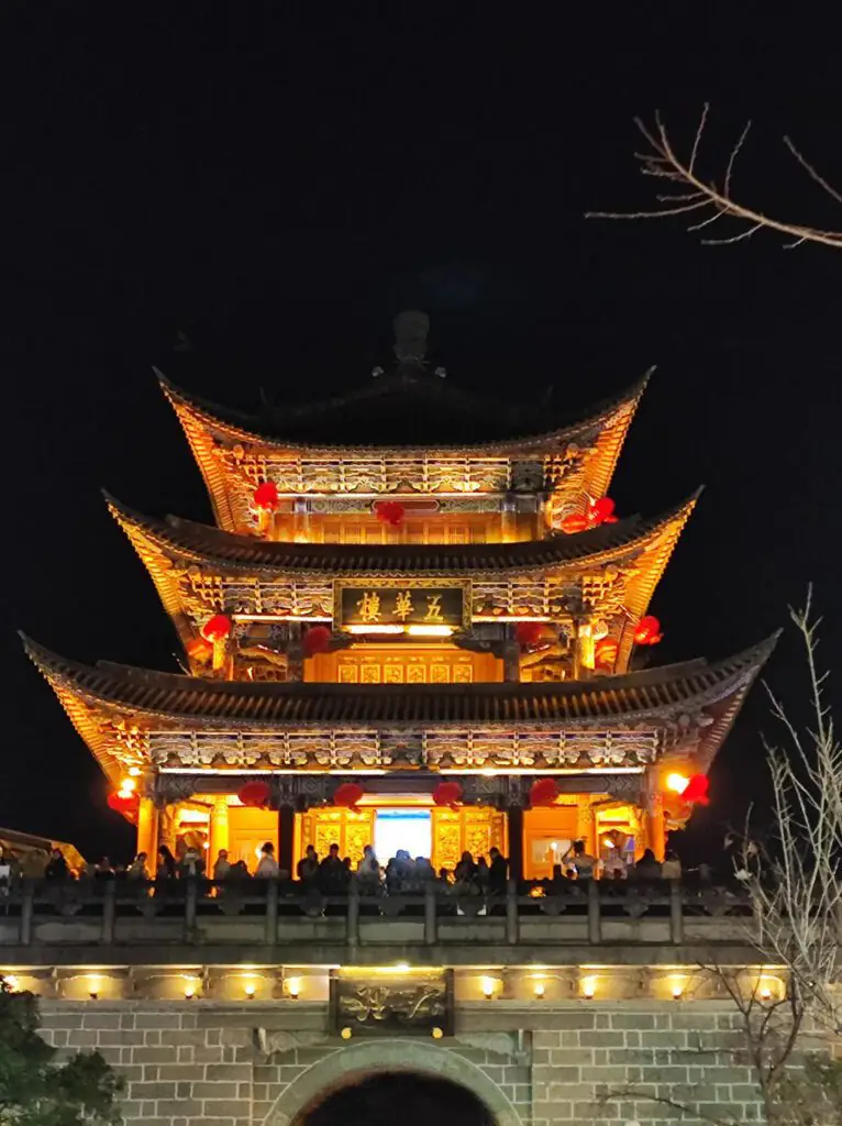雲南旅遊推薦|昆大麗瀘沽湖8日深度慢遊,最值得的雲南行程|國旅環球-China2Go 夜晚燈火下的雲南大理古城街景,青瓦白牆與木雕門窗在暖黃燈光映照下細緻呈現,水道穿行巷間,遊客悠閒漫步