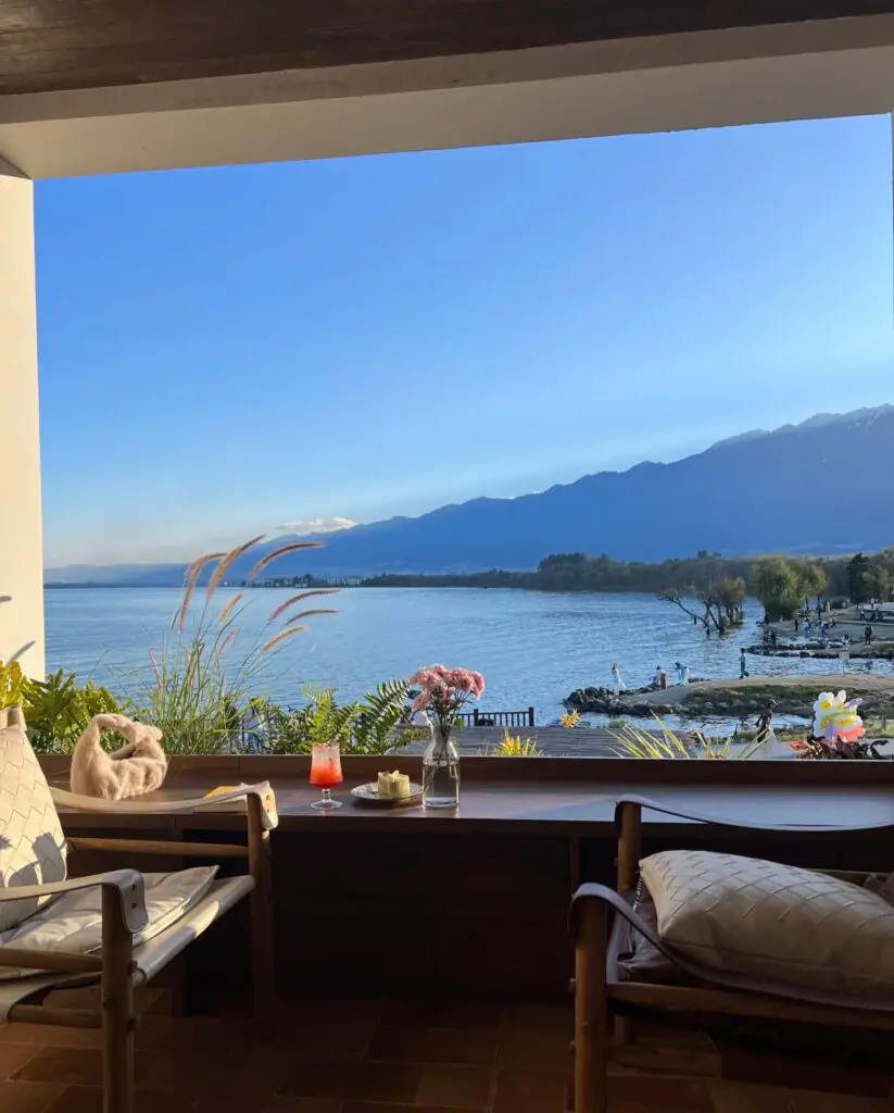 雲南旅遊推薦|昆大麗瀘沽湖8日深度慢遊,最值得的雲南行程|國旅環球-China2Go 遊客在雲南大理洱海生態廊道湖畔享用下午茶,眺望湖面與蒼山,桌上茶點精緻,背景為遼闊的洱海藍天白雲
