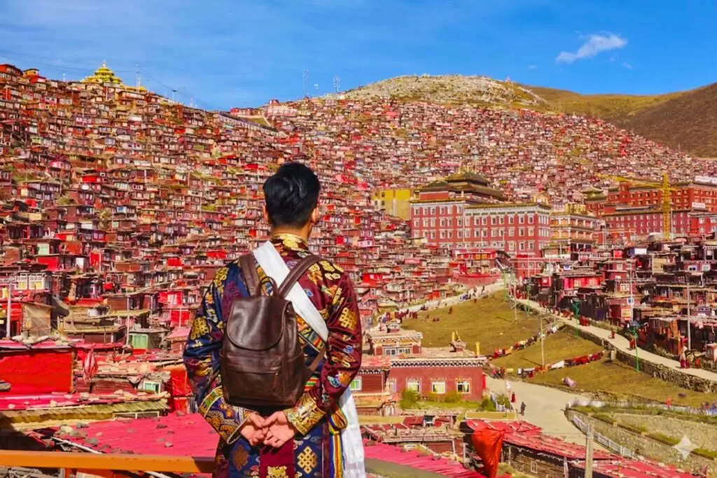 旅客参加国旅环球川西旅行团在俯瞰色达喇荣五明佛学院全景,数万间绛红色木屋依山层叠,四川甘孜藏区